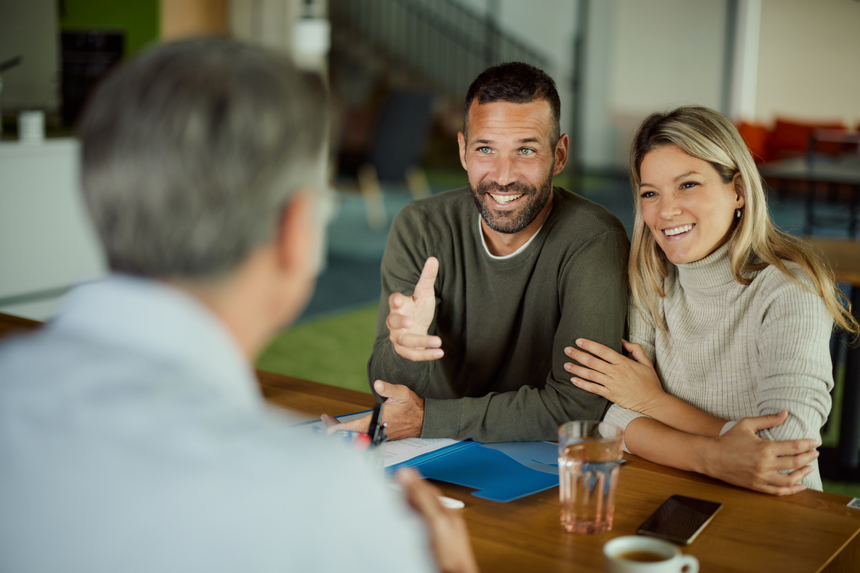 A financial advisor listens to a smiling couple about managing their finances.